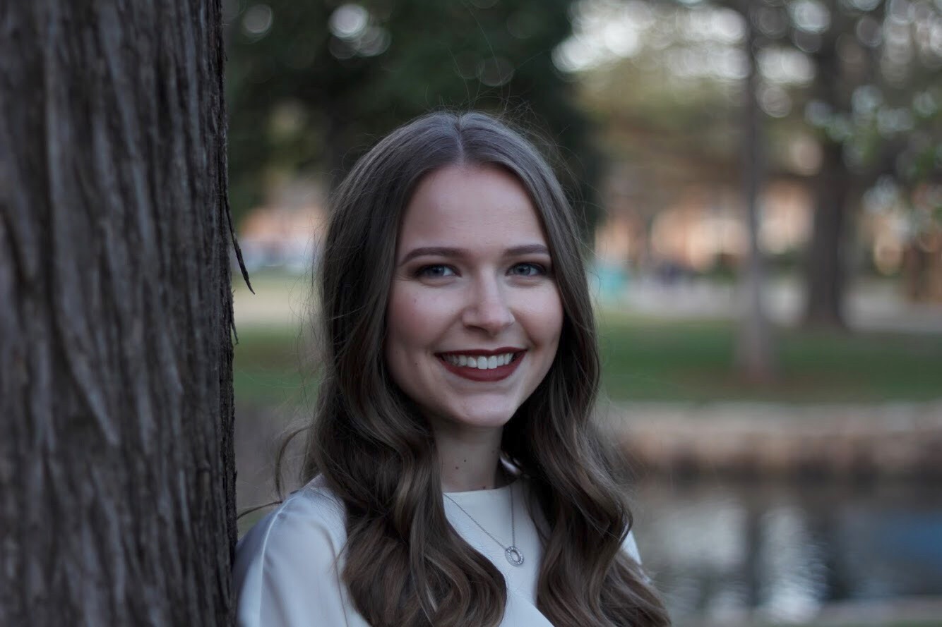 2018 Oklahoma State University Alumna, Emily Sanders, poses by a tree.